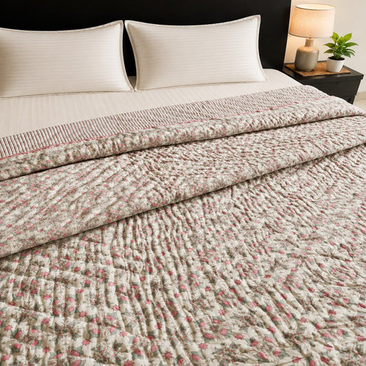A reversible Jaipuri razai/quilt/comforter with a pink floral pattern, styled on a bed with cream pillows and a bedside lamp.
