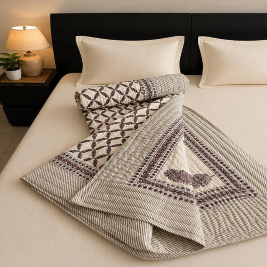 A folded Jaipuri Razai with a lovely geometric diamond pattern in off-white and burgundy, styled on a bed with cream pillows and a dark headboard.
