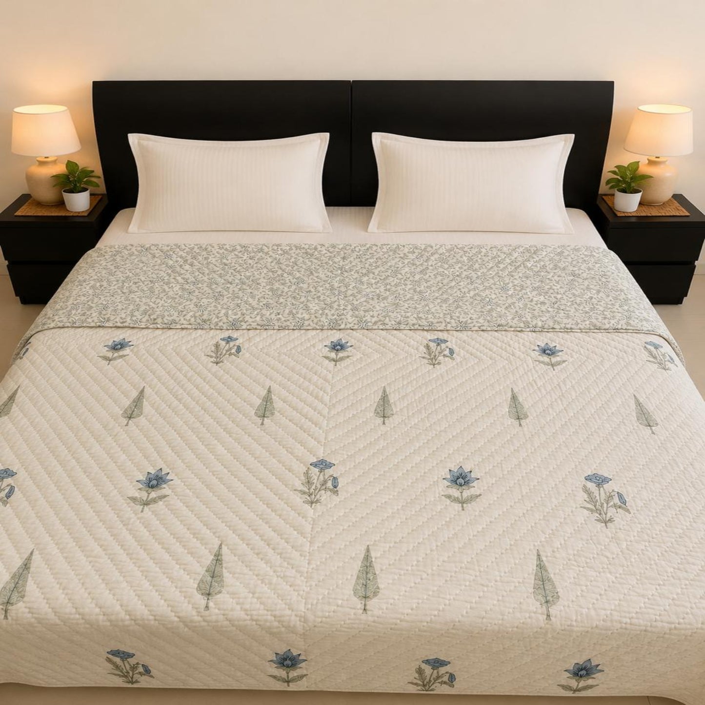 A neatly made bed featuring a blue floral and green tree pattern, a matching patterned throw across the middle, two white pillows, and a dark brown headboard. Two bedside tables with lit lamps and small plants sit on either side.