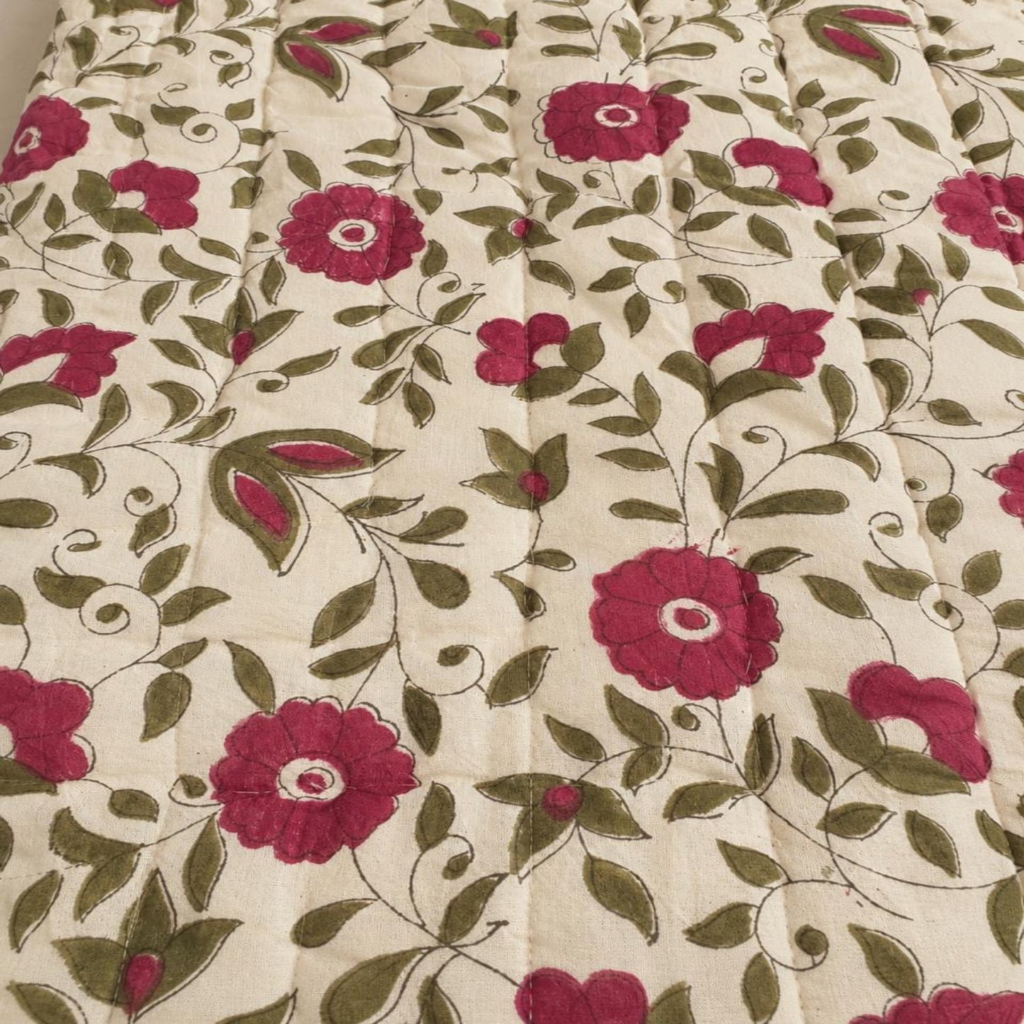 A close-up of a beautiful Jaipuri razai featuring a floral pattern with  pink flowers and olive green leaves on an off-white background.