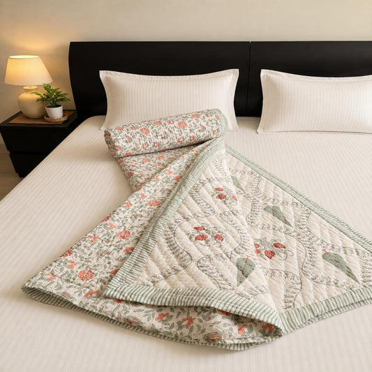 A lovely floral pattern in muted  pink and green,, folded on a bed with white bedding and a dark headboard.