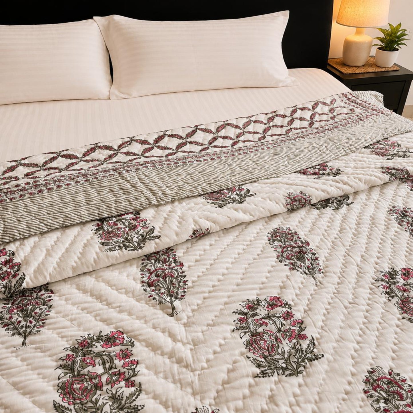 A Jaipuri razai/comforter/quilt on a bed, featuring a muted floral pattern in dusty pink and olive green and a matching striped pillow shams.