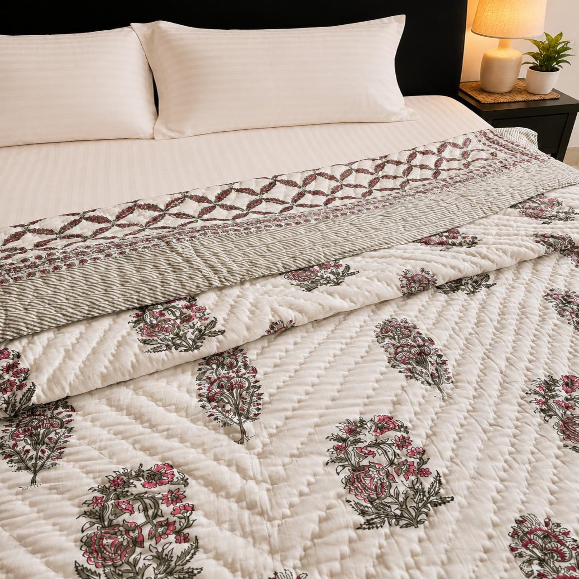 A Jaipuri razai/comforter/quilt on a bed, featuring a muted floral pattern in dusty pink and olive green and a matching striped pillow shams.