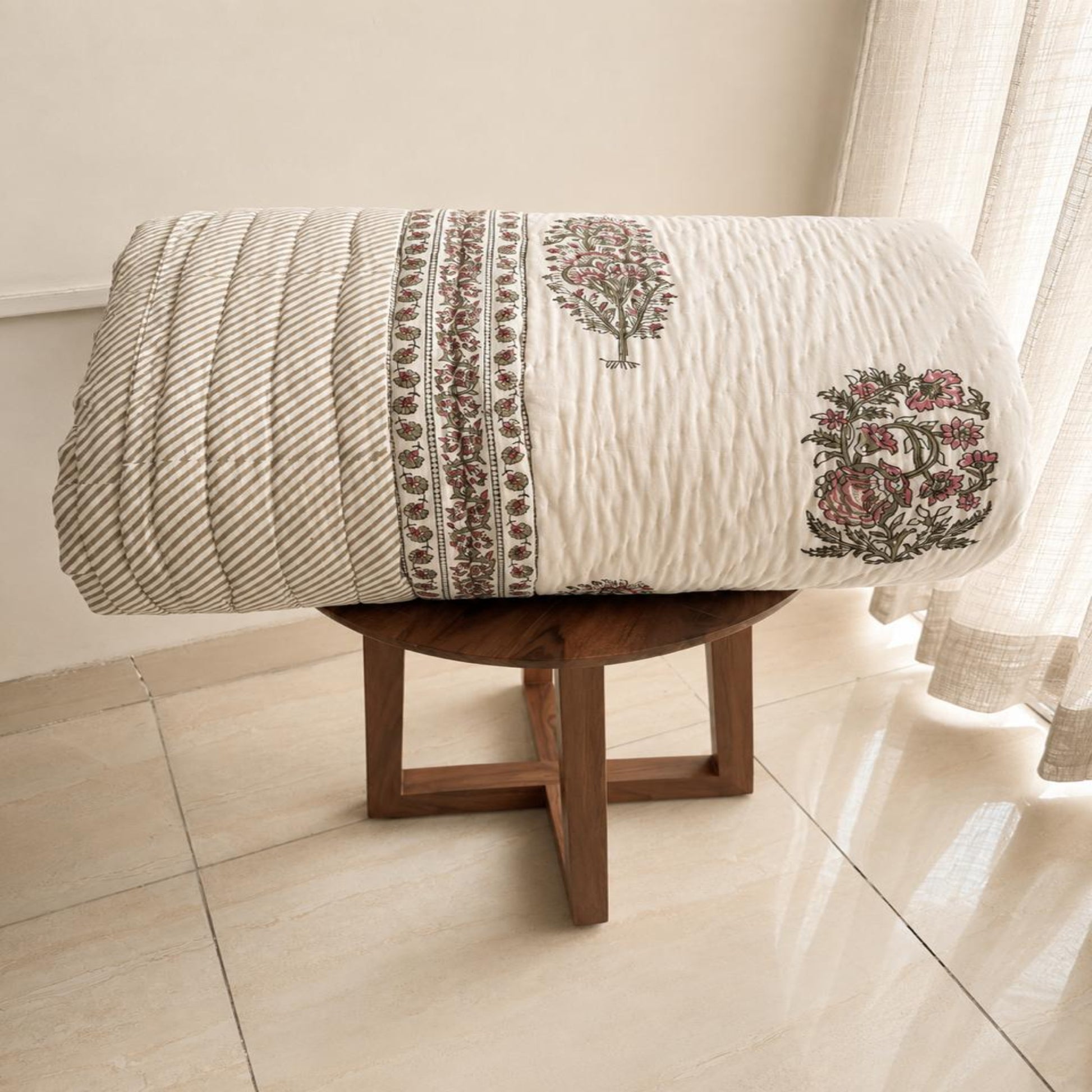A folded beautiful Jaipuri Razai/Comforter/Quilt, displayed on a small wooden stool in a bright room.