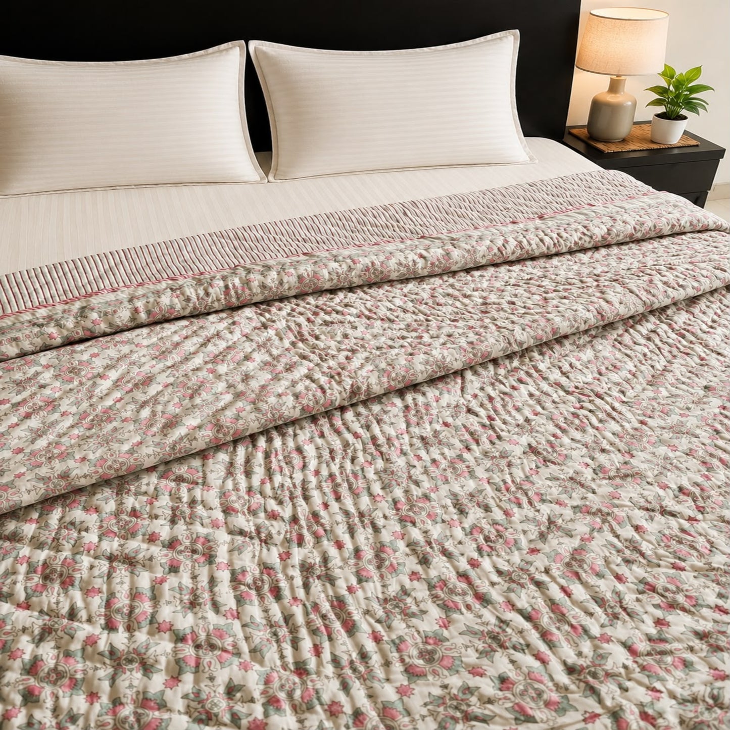 A reversible Jaipuri razai/quilt/comforter with a pink floral pattern, styled on a bed with cream pillows and a bedside lamp.