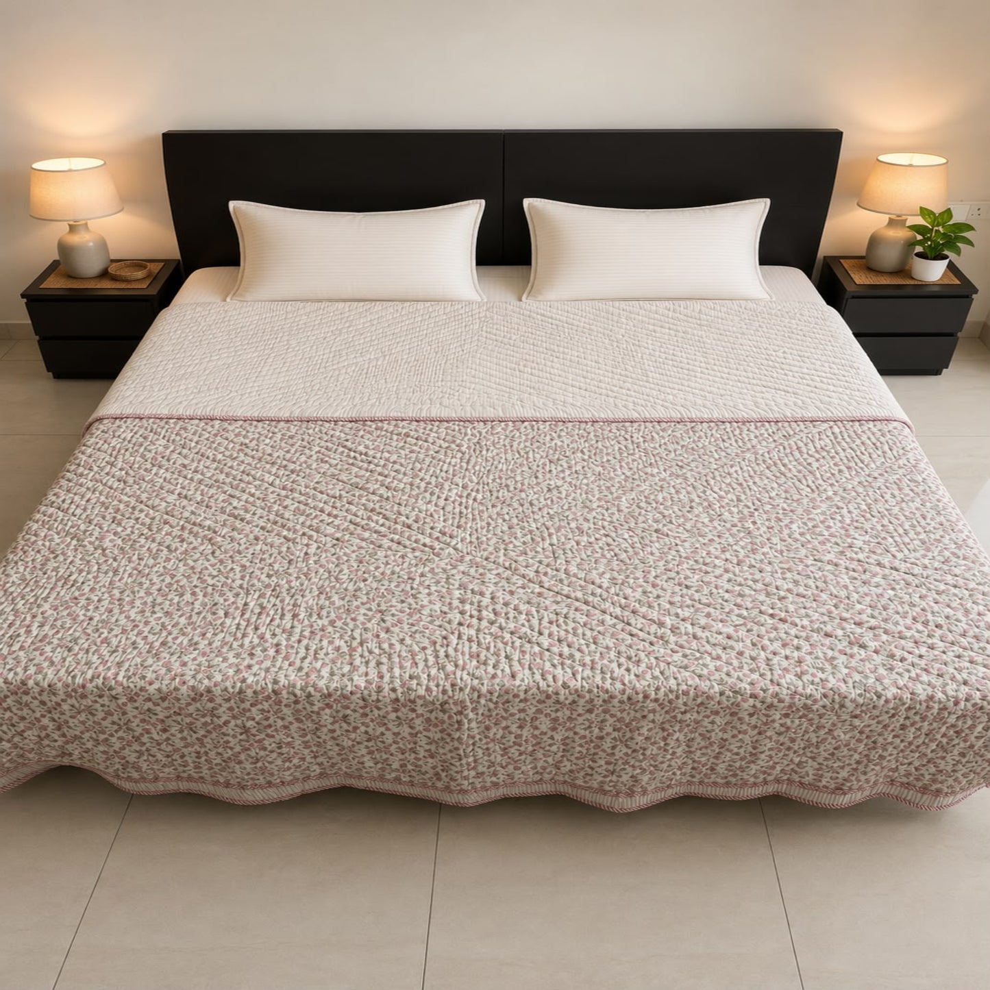 A neatly made bed with an elegant pink patterned Jaipuri razai/comforter/quilt, two white pillows, and a dark headboard, flanked by matching bedside tables with lit lamps.