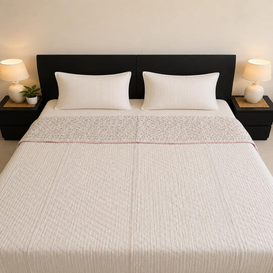 A neatly made bed with a beautiful stripes Jaipuri Razai, having a subtle pin stripes pattern, set against a dark brown headboard with bedside tables and lamps.
