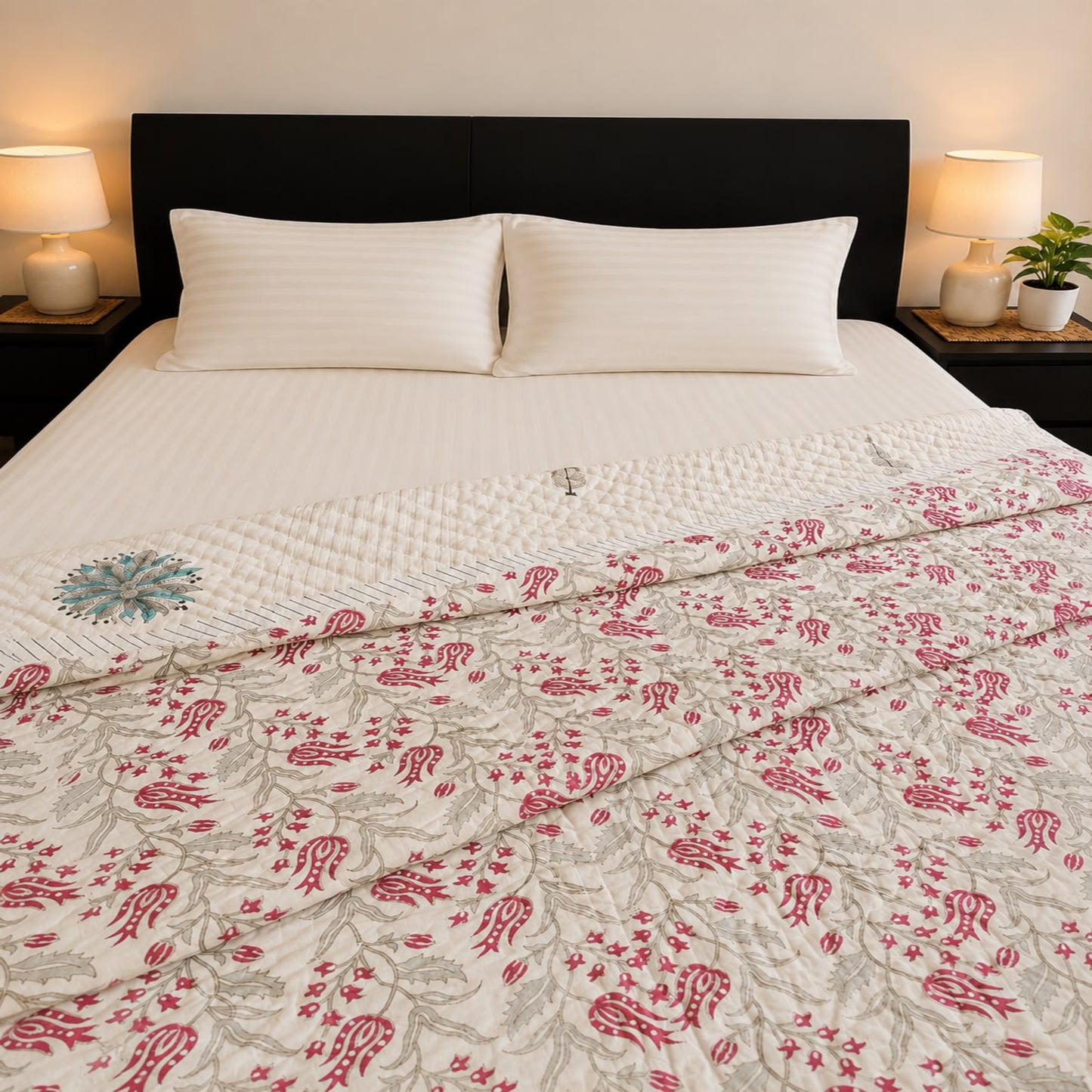 A neatly made bed with white bedding and a reversible Jaipuri razai/comforter/quilt featuring a pink floral and botanical pattern, styled in a bedroom setting with bedside lamps and a dark brown headboard.