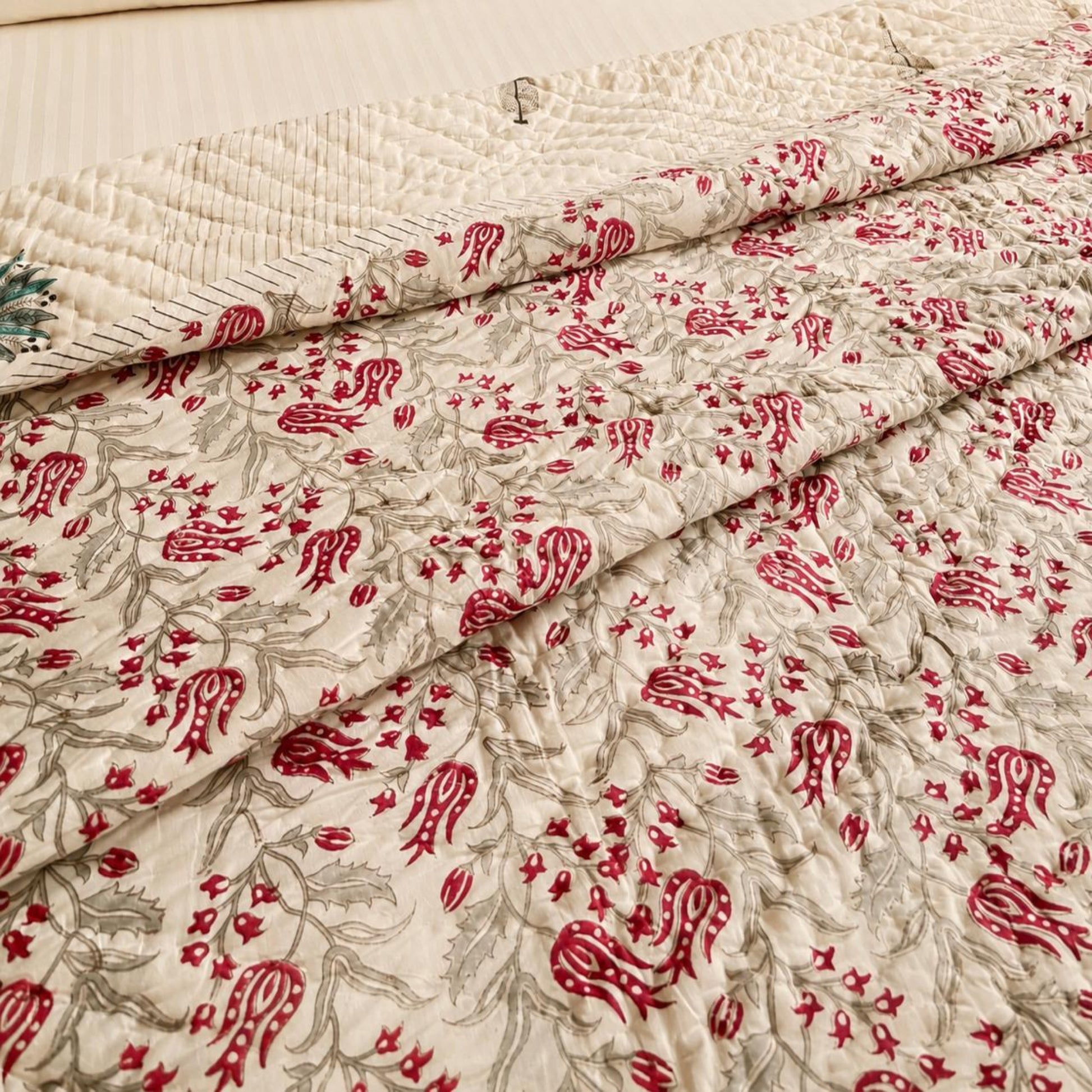 A close-up of Razai/comforter with an off-white background and an allover red and gray floral print. The fabric is folded to show both the patterned front and a smoother off-white back panel.