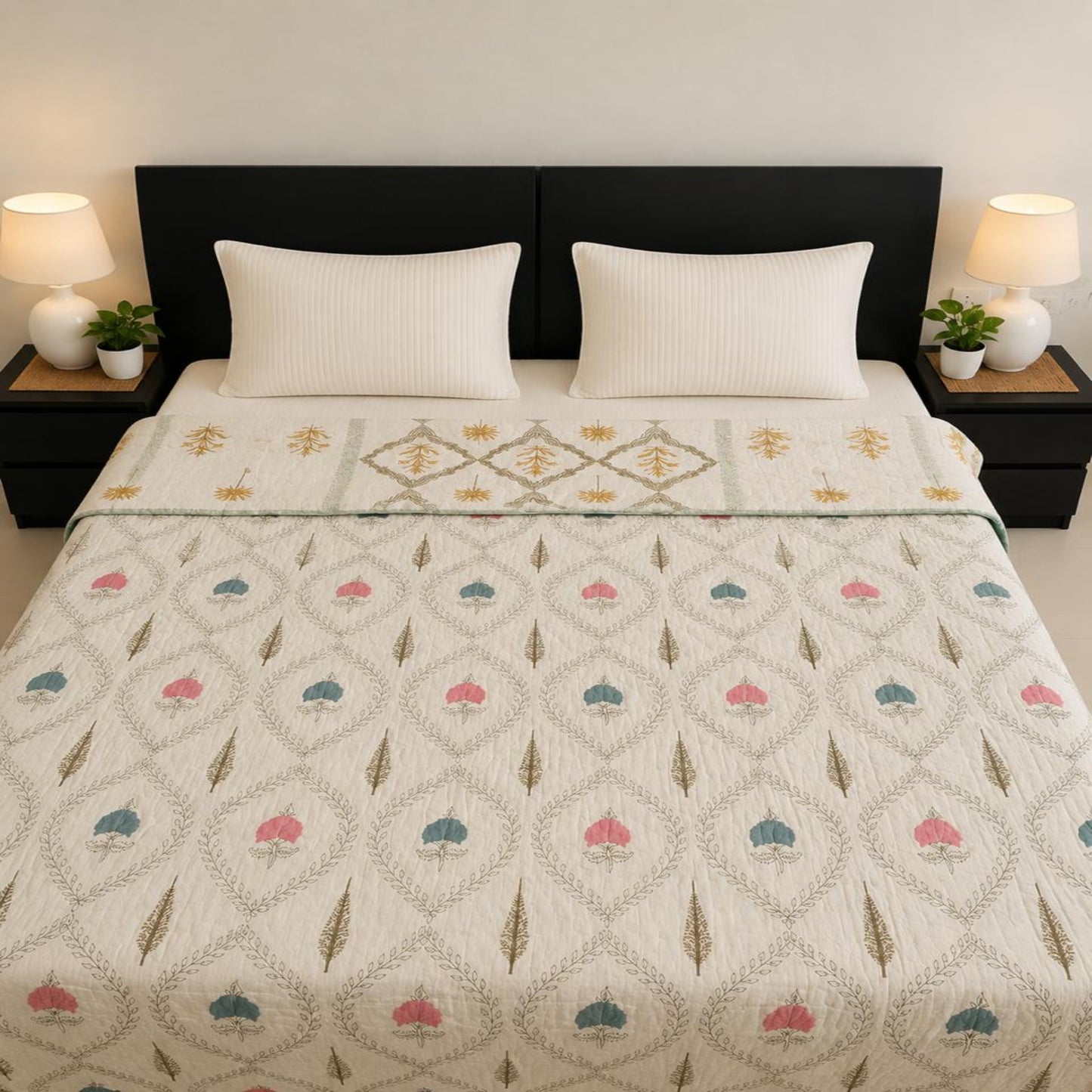 A neatly made bed in a bedroom setting, featuring a multi coloured Jaipuri Razai with a geometric diamond pattern and small pink, blue, and gold motifs. Two white pillows and a dark brown headboard are visible, flanked by matching black nightstands with lit lamps and small potted plants.