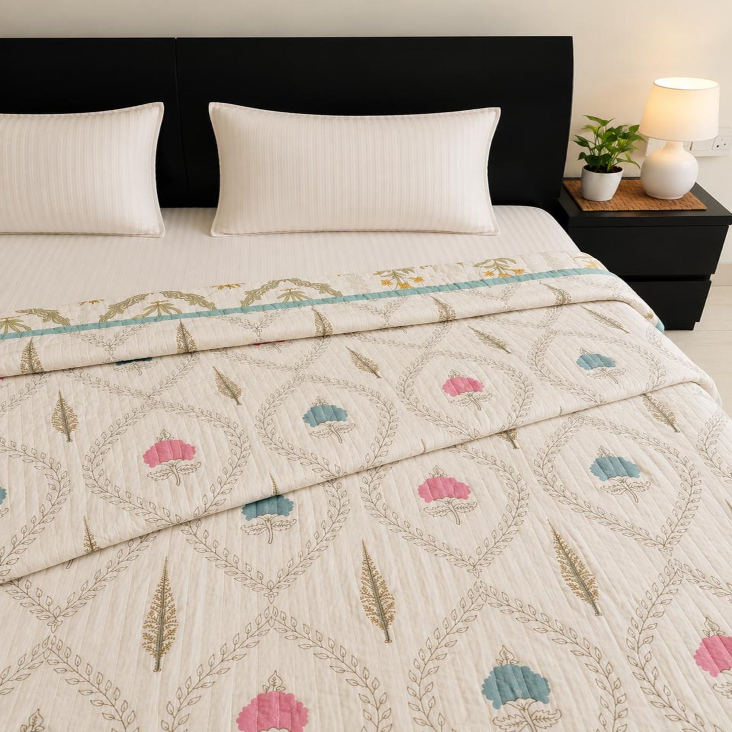 A lovely razai/quilt/comforter with a geometric leaf pattern and pink, blue, and gold motifs, styled on a bed with two white pillows and a dark brown headboard.