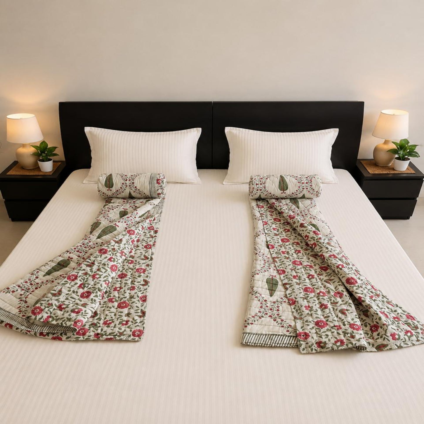 A neatly made bed with a pair of floral and paisley patterned Jaipuri Razai/Quilt/Comforter and coordinating pillow shams, styled in a symmetric bedroom setting with bedside lamps and plants.