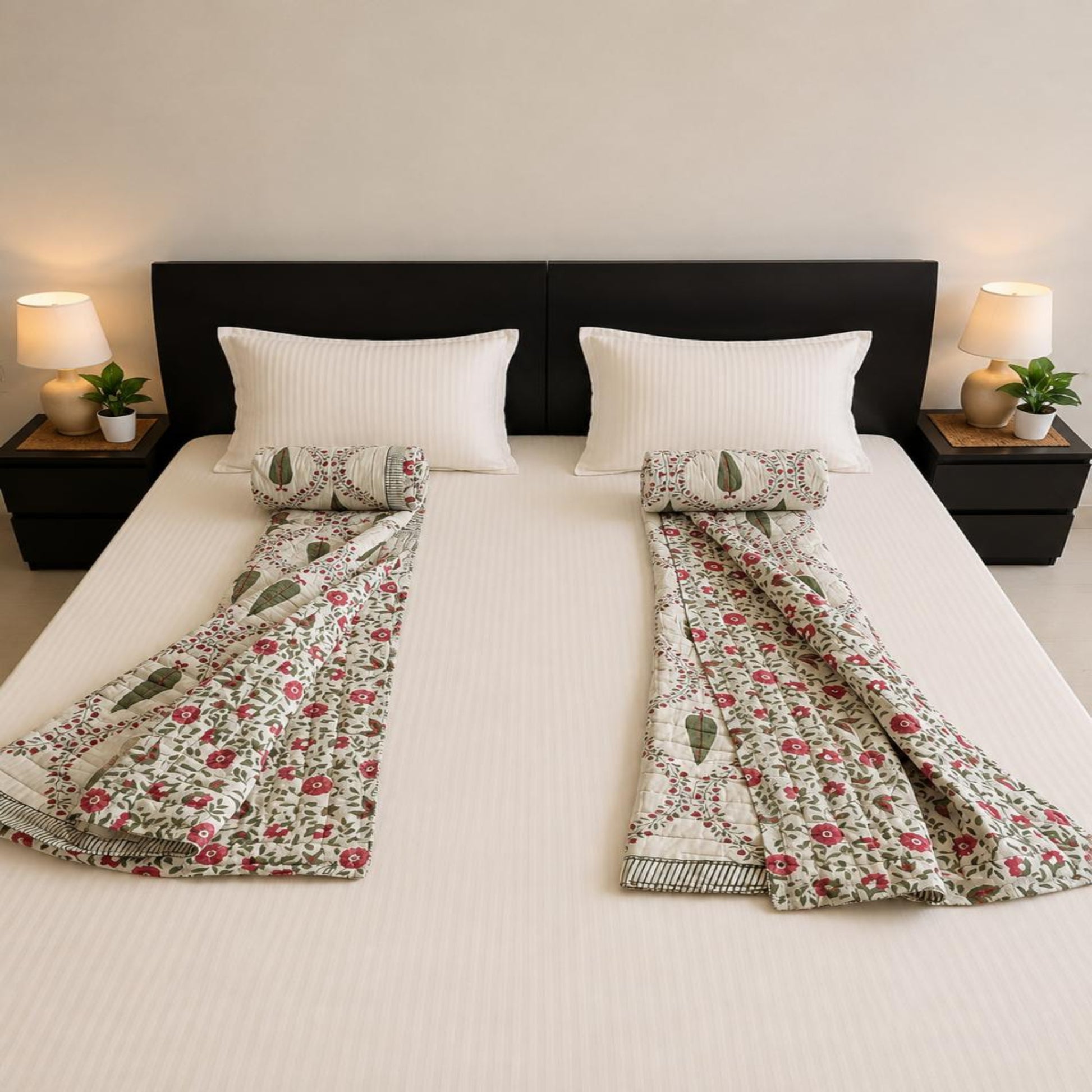 A neatly made bed with a pair of floral and paisley patterned Jaipuri Razai/Quilt/Comforter and coordinating pillow shams, styled in a symmetric bedroom setting with bedside lamps and plants.
