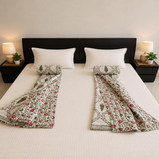 A neatly made bed with a pair of floral and paisley patterned Jaipuri Razai/Quilt/Comforter and coordinating pillow shams, styled in a symmetric bedroom setting with bedside lamps and plants.