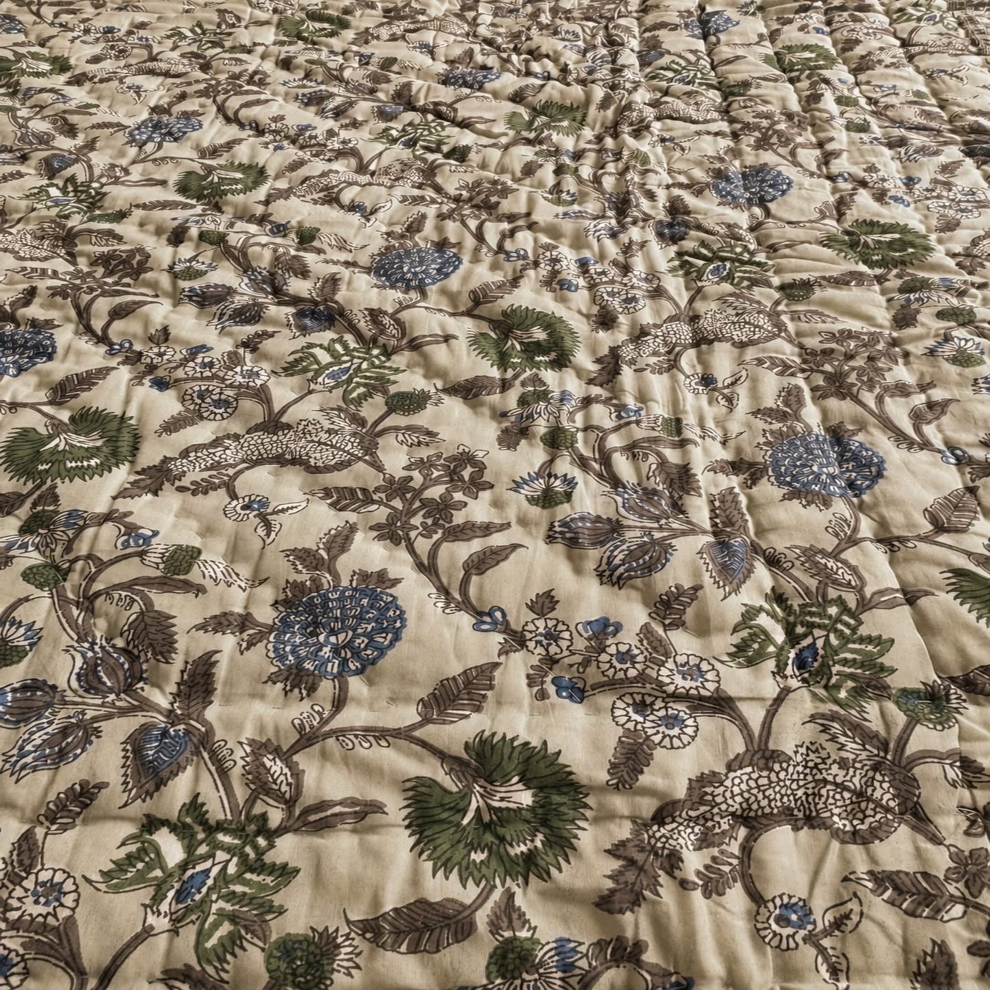 A close-up of a with an all-over floral and botanical print on a warm beige background, featuring green, blue, and brown botanical motifs.
