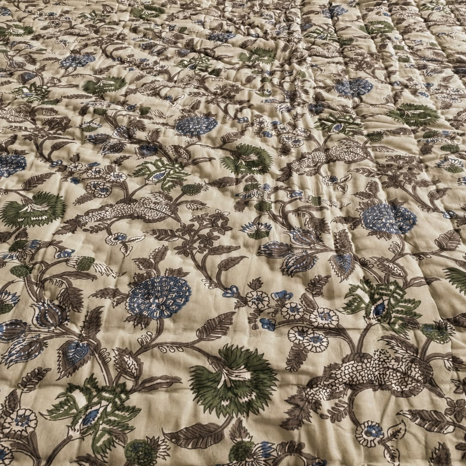A close-up of a with an all-over floral and botanical print on a warm beige background, featuring green, blue, and brown botanical motifs.