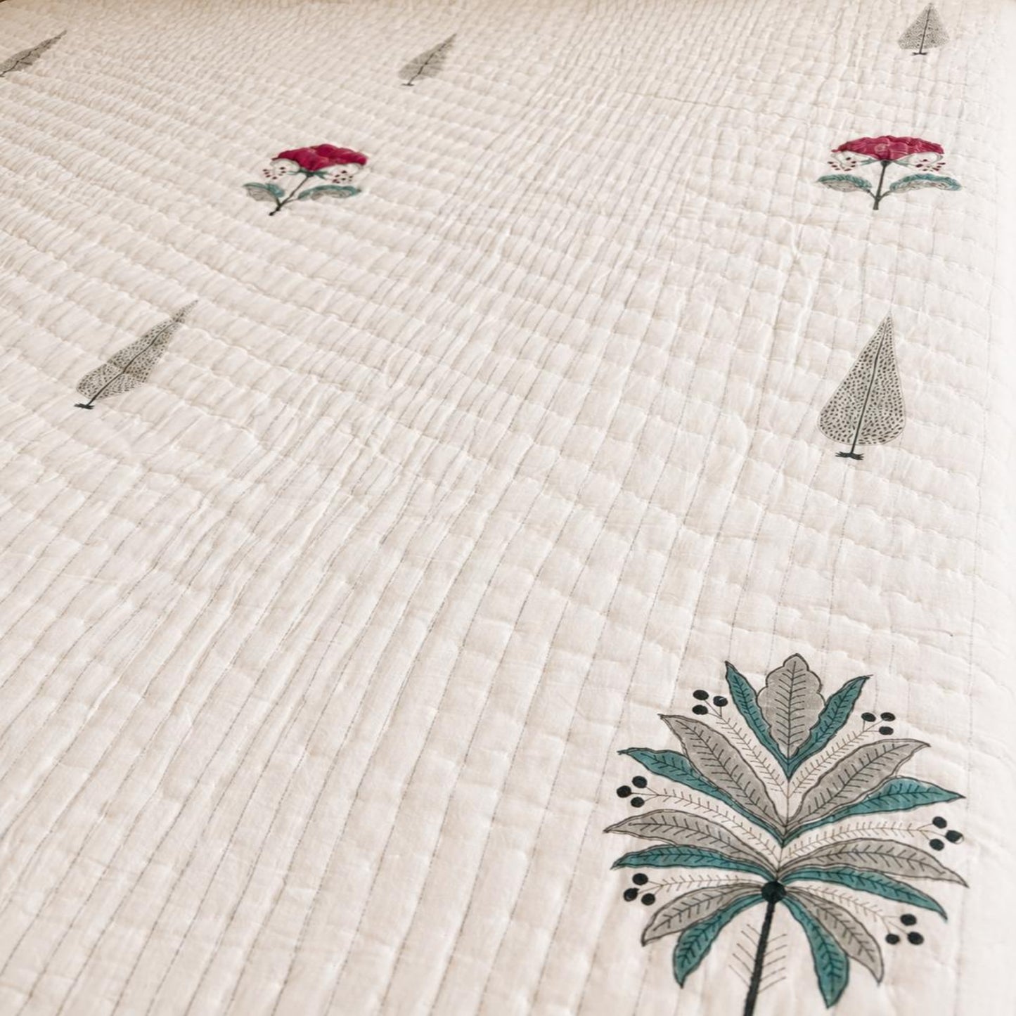A close-up of a beautiful Jaipuri Razai with tropical motifs, including a large palm leaf and smaller floral and tree designs in teal, gray, and red.