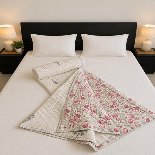 A beautiful Jaipuri Razai, styled on a bed with white pillows and sheets, flanked by matching rolled and folded sections.