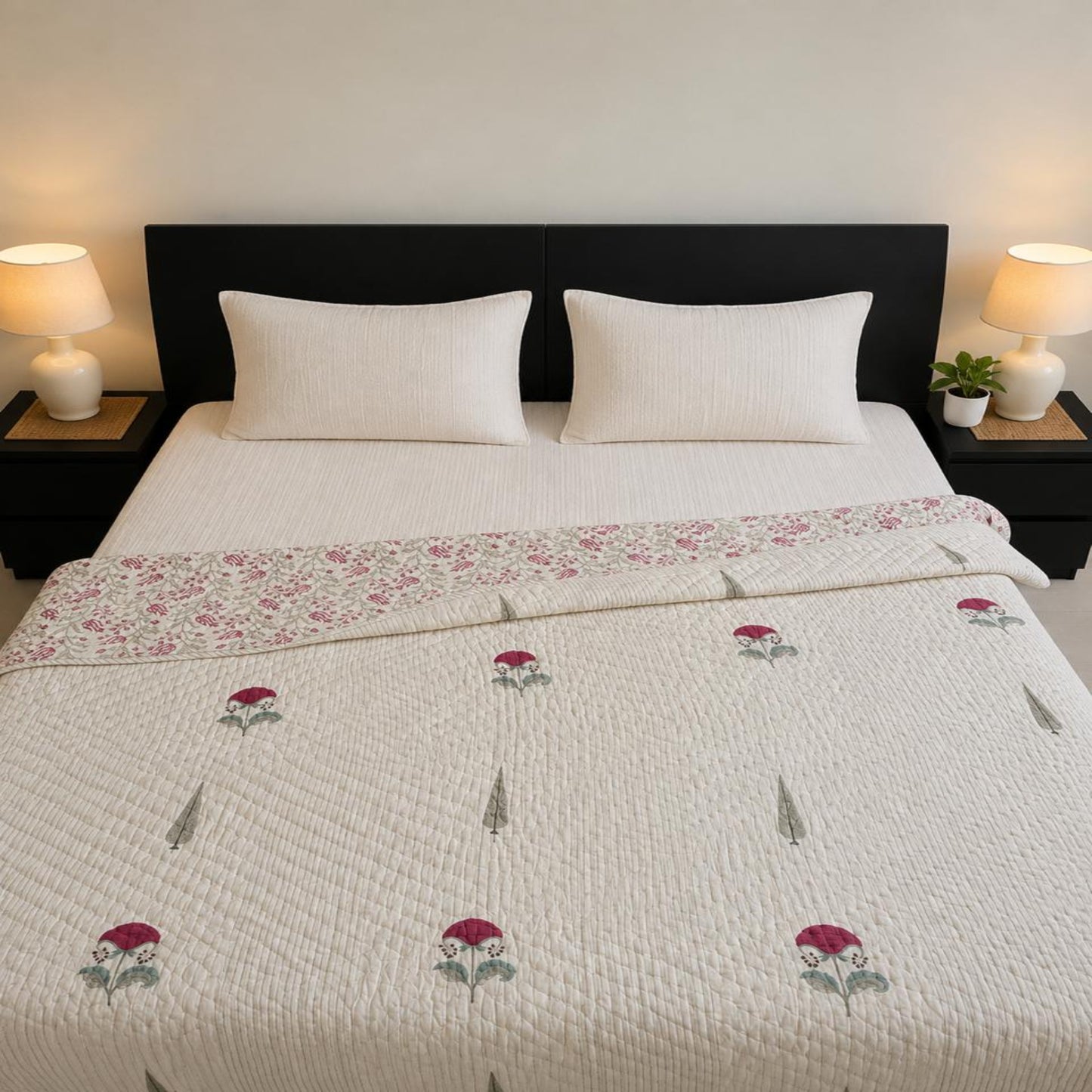 A lovely Jaipuri Block Print Razai/Quilt/Comforter with red and green rose motifs, styled on a bed with two white pillows and flanked by bedside lamps.