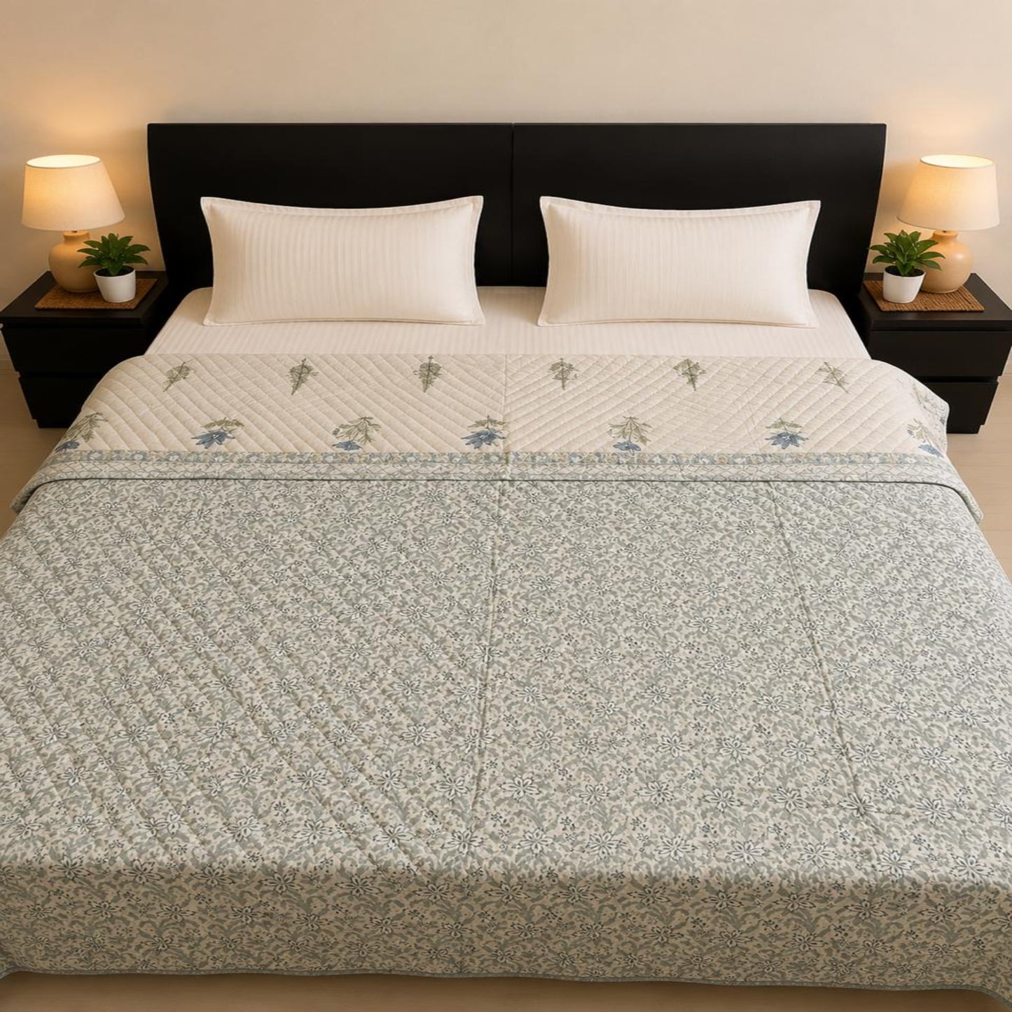 A neatly made bed with indigo and green floral Jaipuri Razai/quilt/comforter, white pillows, and a white sheet, set against a dark wood headboard with bedside lamps and plants.
