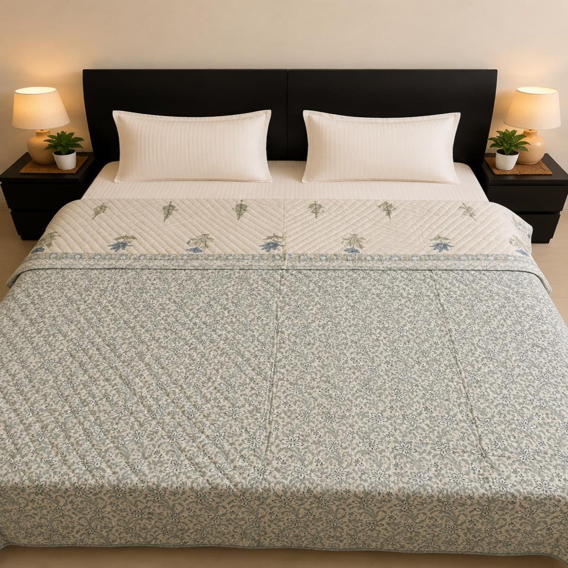A neatly made bed with indigo and green floral Jaipuri Razai/quilt/comforter, white pillows, and a white sheet, set against a dark wood headboard with bedside lamps and plants.